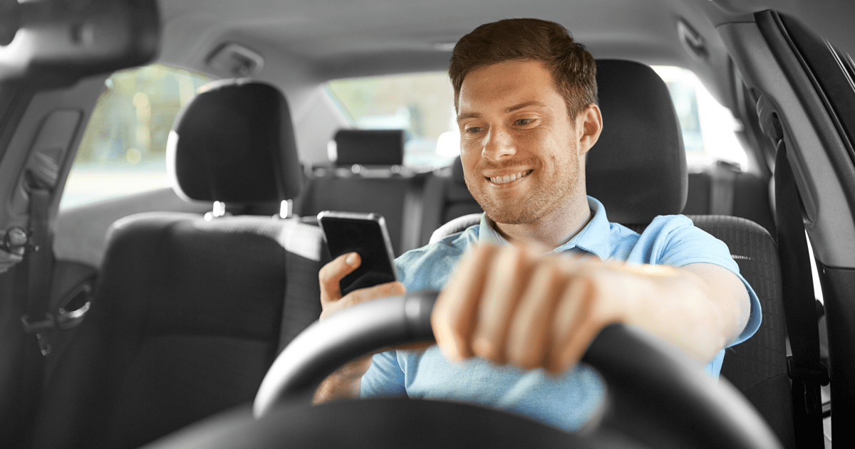 Een man is in een auto aan het rijden en grbuikt tijdens het rijden zijn mobiele telefoon